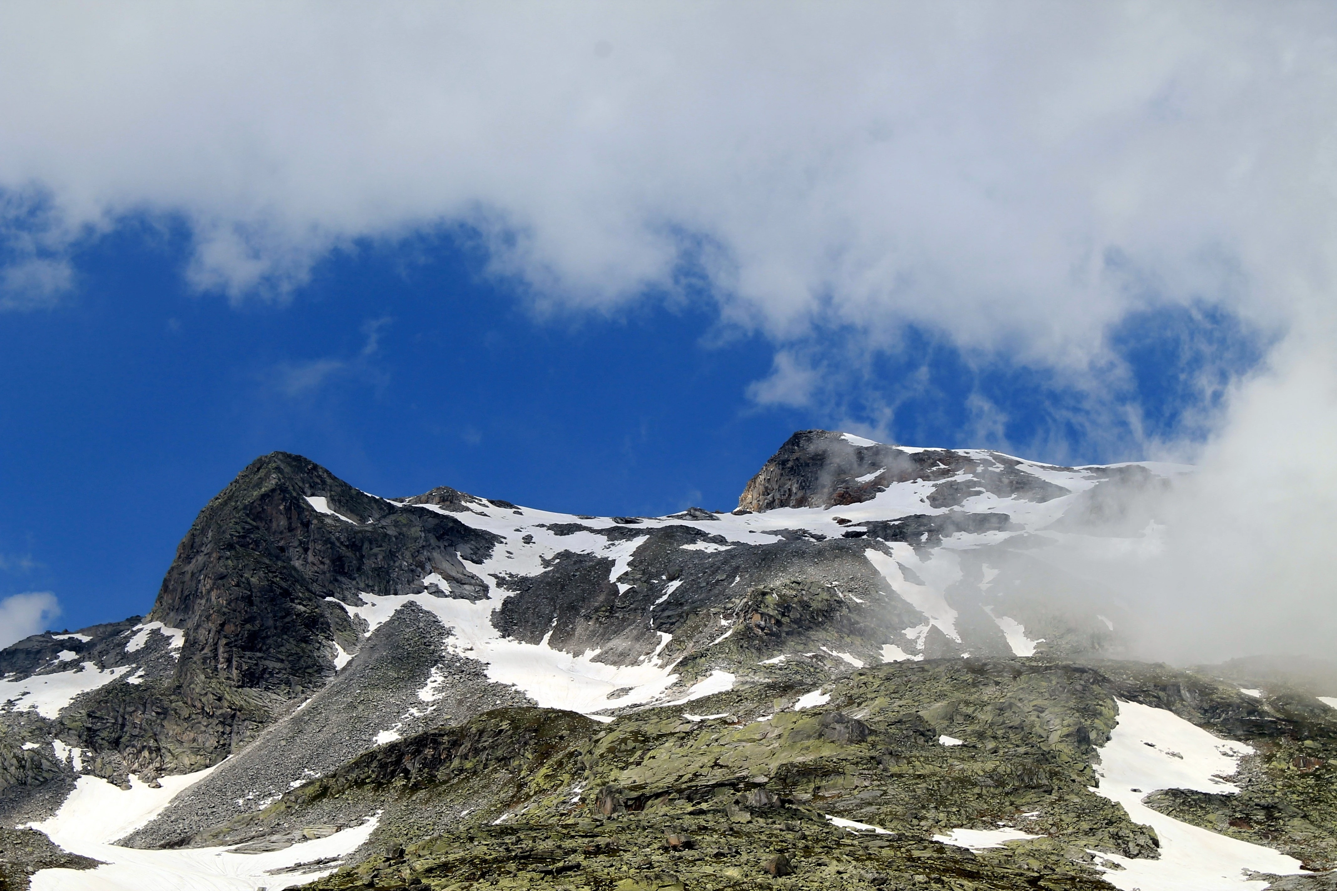 Skalnaté svahy se sněhem, mraky se trhají a odhalují modré nebe