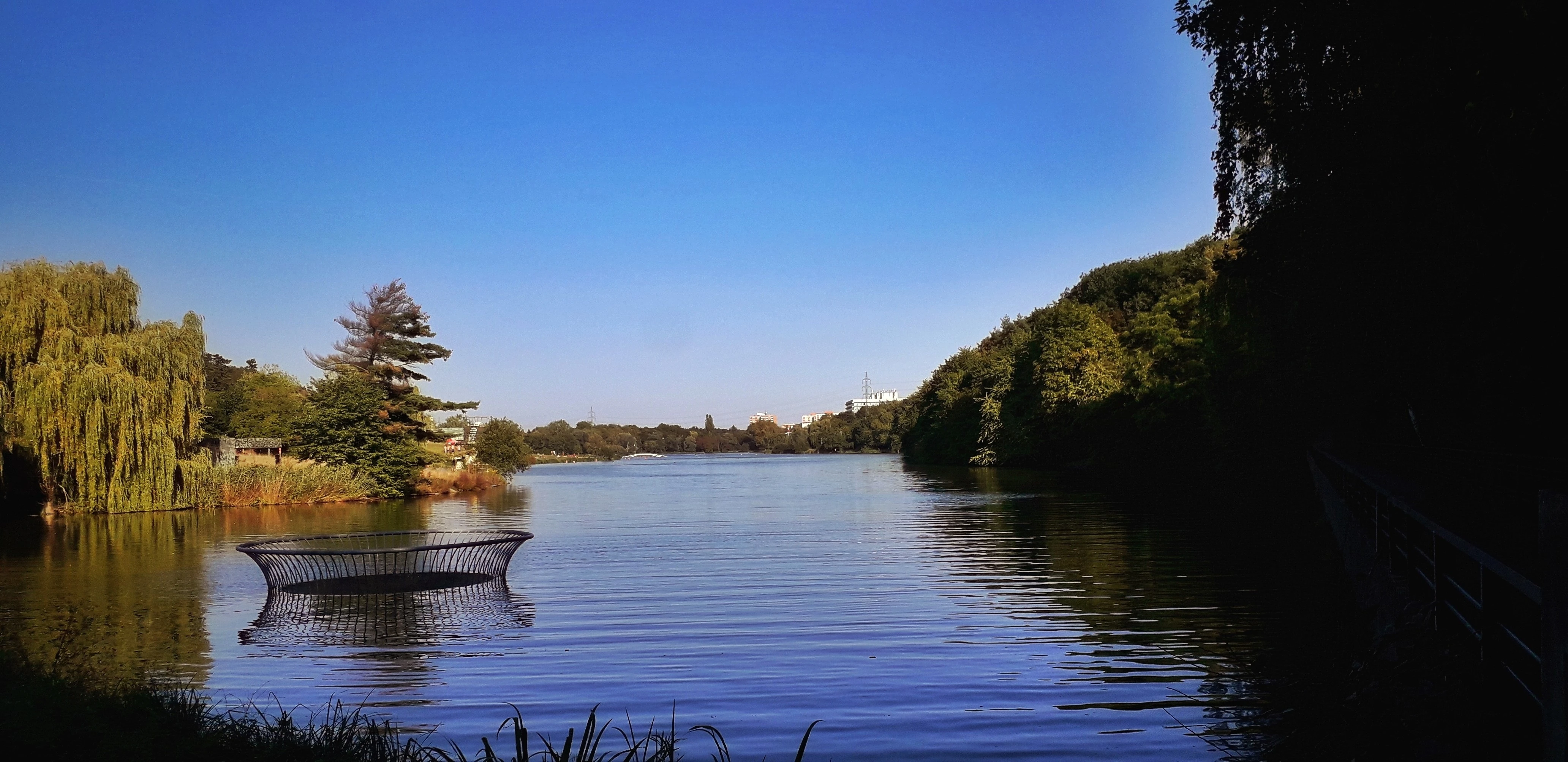 Řeka s uměleckým objektem na hladině, břehy se stromy, měkké světlo