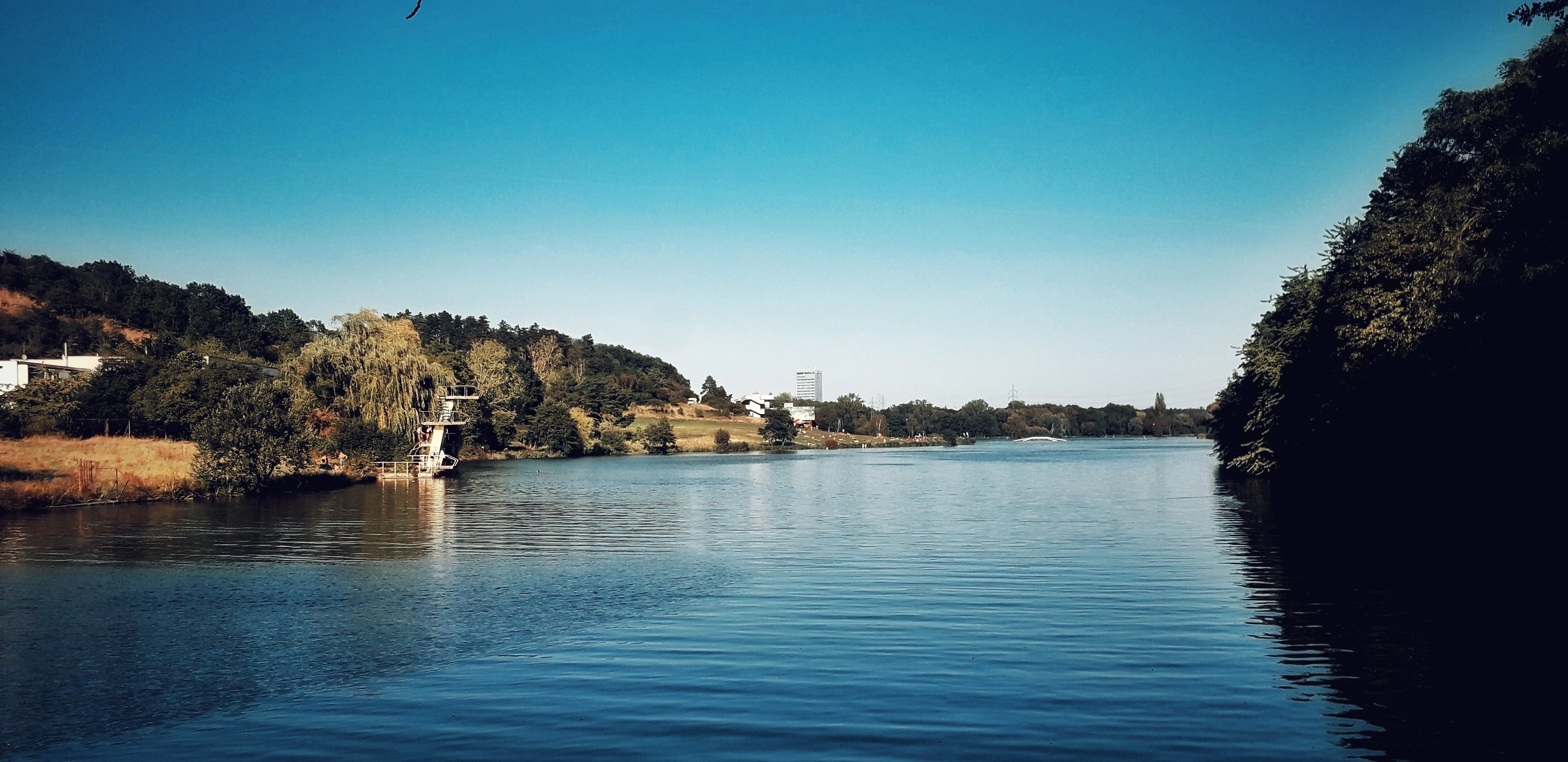 Záliv s vodou a skokanskou věží, v pozadí město a stromy