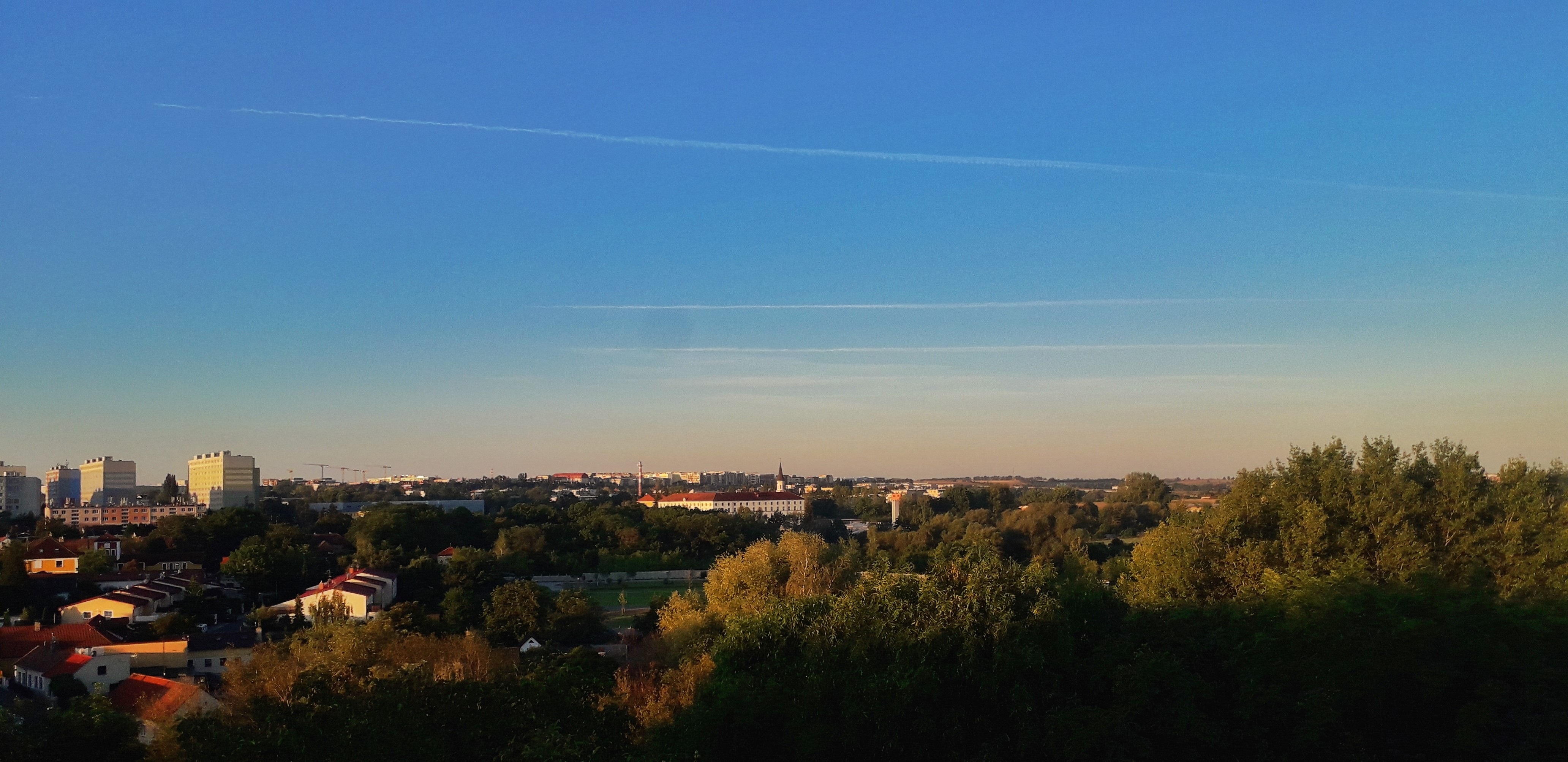 Široký panoramatický výhled přes zeleň na město a rovinu za ním